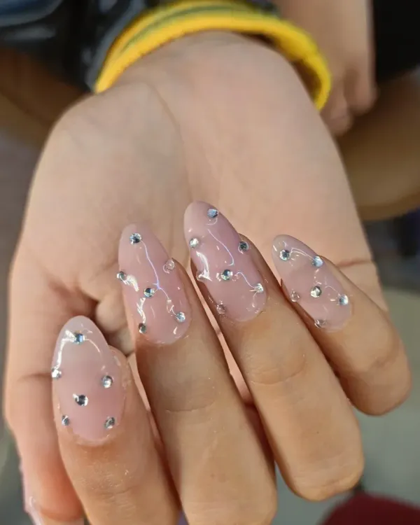 A simple yet stunning look. These long, almond-shaped extensions have a sheer pink base and are adorned with scattered silver rhinestones for a "diamond rain" effect.