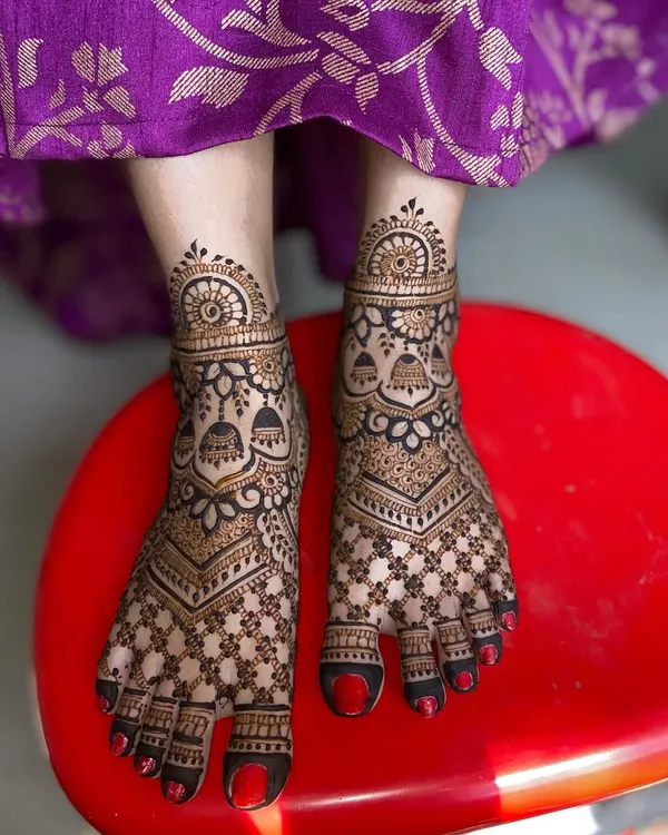 A full-coverage bridal foot mehandi design featuring a dense checkerboard pattern, floral details, and hanging jhumka motifs.