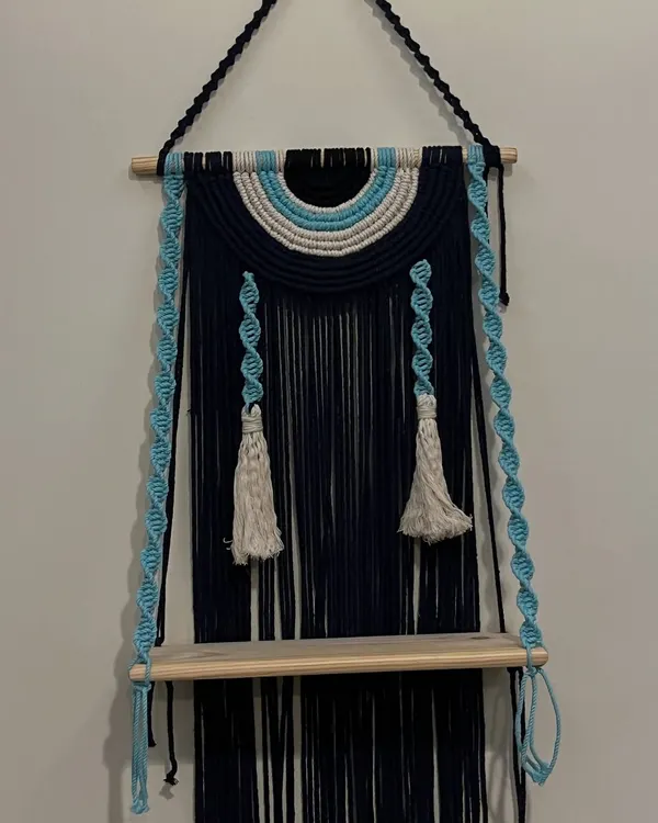I love creating pieces that are both beautiful and useful. This evil eye themed wall shelf does just that, combining a protective symbol with a practical wooden shelf. The deep navy blue and sky blue cords with twisted hangers make it a unique piece.