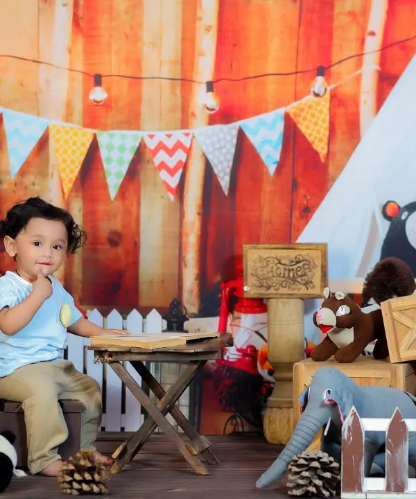 A one-year-old enjoying our rustic wood cafe theme, sitting at a small table in a cozy, camp-like setting with string lights and stuffed animals.