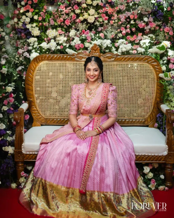 This grand Kanchi lehenga, transformed from a traditional saree, is a perfect example of how we can blend heritage with contemporary bridal style. The voluminous light pink skirt with its classic gold border, paired with a hand-embroidered puff-sleeve blouse, creates a look that is both regal and romantic for your big day.