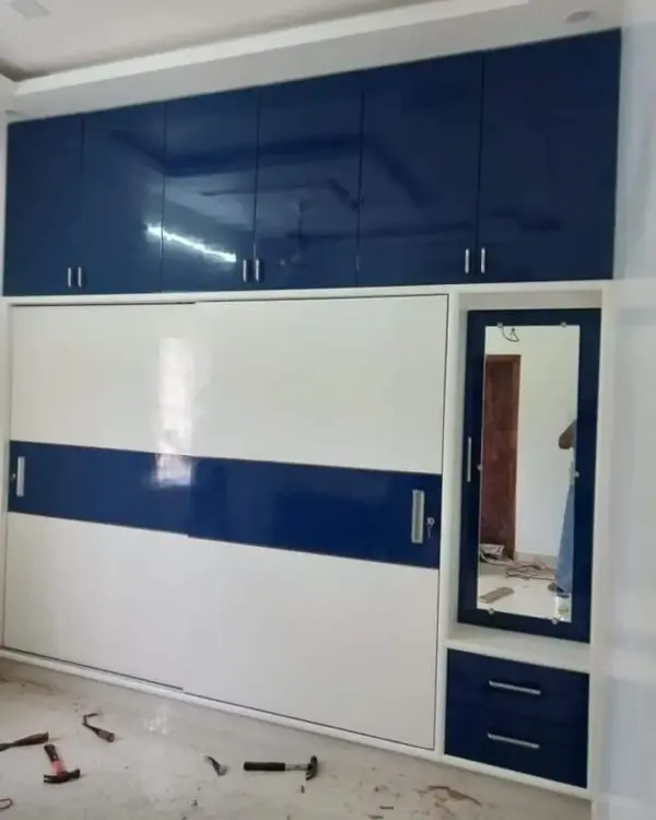 A floor-to-ceiling wardrobe with a bold blue and white high-gloss finish. This design combines sliding doors for the main section with a separate dressing mirror unit and upper loft cabinets for extra storage.