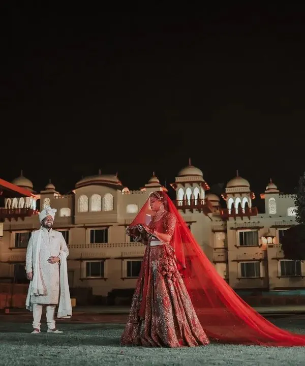 A night shot at a heritage hotel, with the bride's stunning red veil creating a dramatic and royal frame. This is a perfect example of a luxury wedding portrait that feels both grand and intimate.