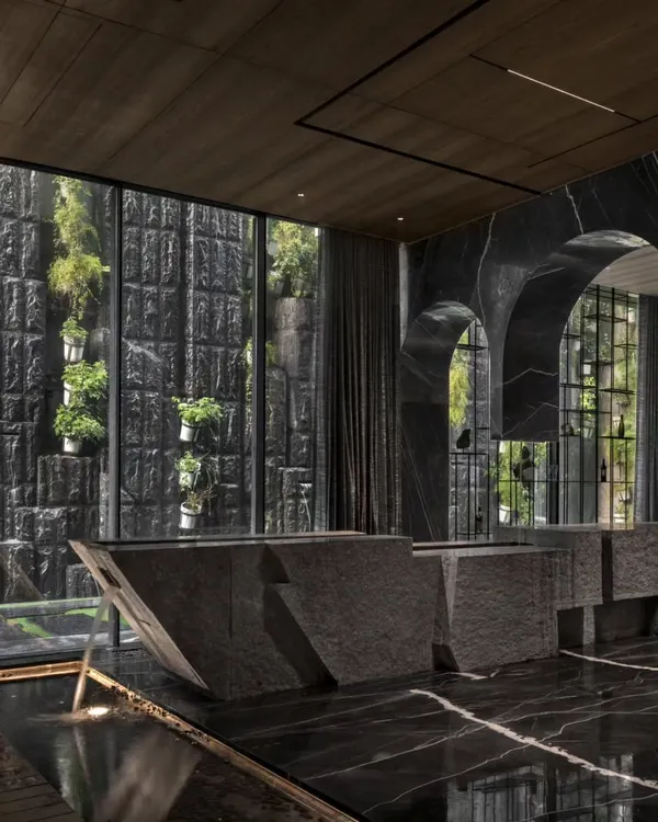 This super-luxury home is a perfect blend of opulent architecture and nature. A monolithic stone bar stands before a full-height window looking out onto a vertical garden, all reflected in the polished black marble floor. This is sustainability at its most luxurious.