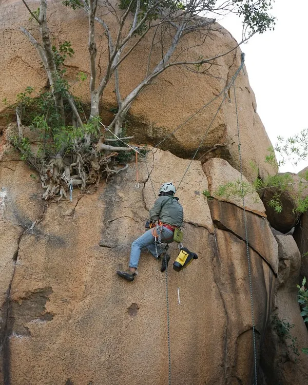 The hard work behind the send. Here, a team member is equipped for route development, a process that involves cleaning the rock and installing permanent safety anchors to create new climbs for the community.