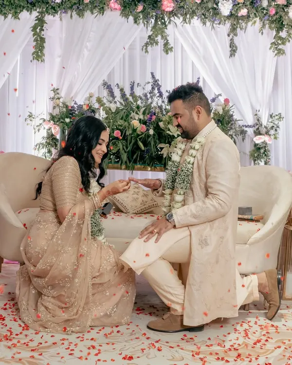 A tender moment during the ring ceremony, with the groom on one knee. The floral decor and scattered petals create a truly romantic setting.