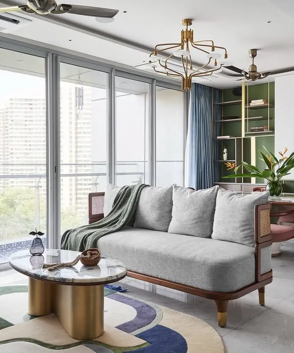 A wide view of the open-concept living room, designed to be bright and welcoming with large French windows overlooking the Aarey colony forest. The space seamlessly integrates living, dining, and kitchen areas with a consistent white marble floor.