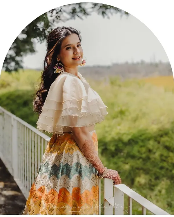 A happy client glowing in her custom-designed chevron lehenga. The organza cape blouse with pearl detailing adds a touch of modern elegance, perfect for a daytime wedding event.