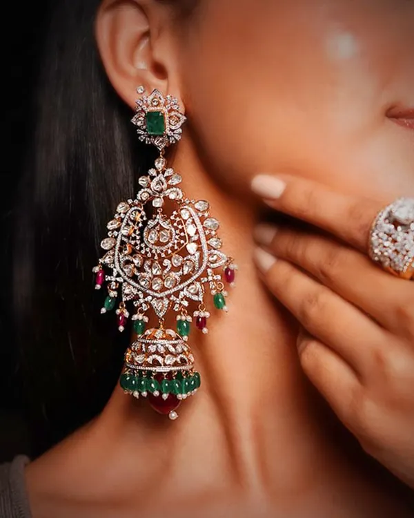 A pair of magnificent bridal earrings, combining traditional jhumka and chandelier styles. The piece features Polki diamonds, vibrant emeralds and rubies, and intricate enamel work, making it a true heirloom.