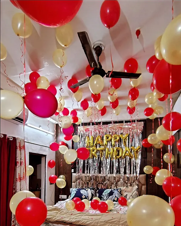 A classic birthday room decoration with red and cream balloons filling the entire space. The setup includes a silver foil curtain behind the bed and 'Happy Birthday' foil balloons to create a festive atmosphere.