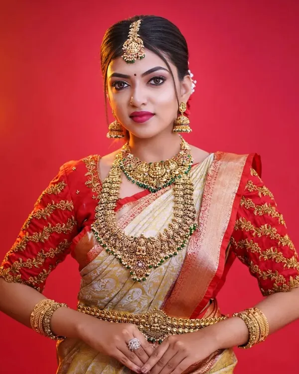 This is the quintessential South Indian bridal look. Our antique finish temple jewellery, including a detailed choker, long haram, and matching jhumkas, perfectly complements the silk saree, creating a timeless and regal appearance for any madve hudgi (bride).