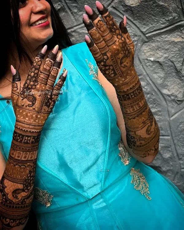 A happy engagement bride showing off her beautifully stained mehendi. The deep brown color looks stunning against her blue dress.