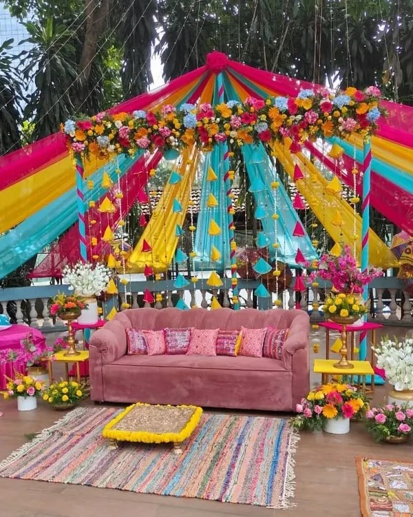 A spectacular Mehendi setup featuring a canopy of vibrant drapes in pink, yellow, and turquoise. The colorful theme is perfect for a lively and joyful daytime celebration.