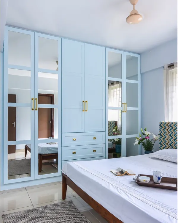 This is one of our most-loved wardrobe designs. The powder blue finish, mirrored panels, and elegant brass handles create a look that is both classic and fresh, while maximizing storage and light.