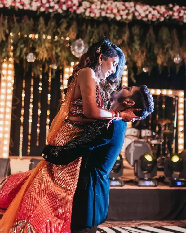 A classic romantic lift on the dance floor during the couple's Sangeet performance. This shot captures the chemistry and joy between the couple against a backdrop of stage lights.