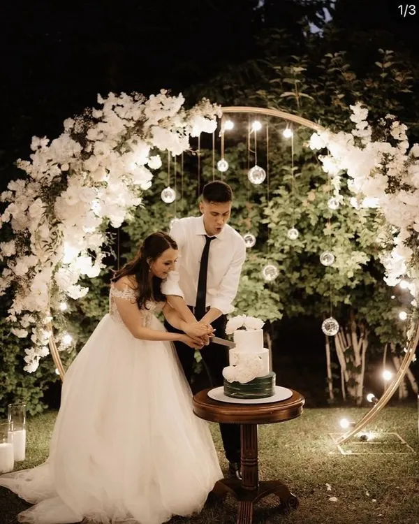 A romantic moment during an outdoor evening engagement. I created a beautiful circular arch with white flowers and hanging glass globes with lights to frame the cake-cutting ceremony.