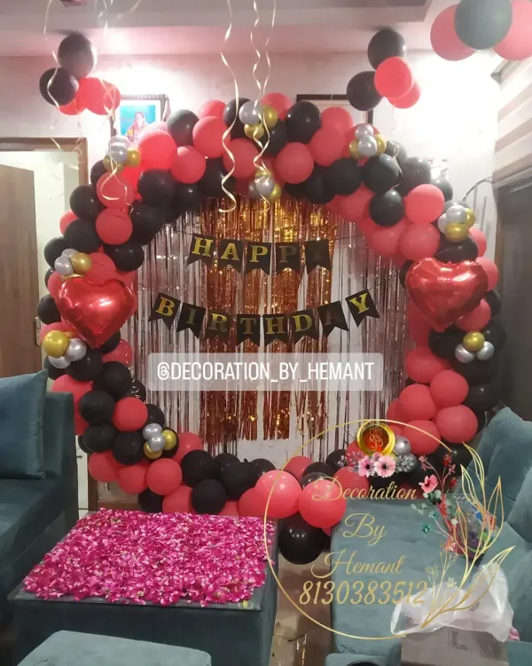 This birthday setup features a bold red and black color scheme. The circular balloon frame, birthday banner, and a table covered in rose petals combine to create a complete party look in your living room.
