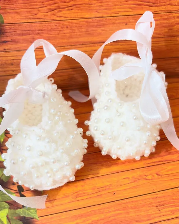 These beautiful white booties are adorned with dozens of tiny pearls and finished with a soft satin ribbon, making them a truly special choice for a baptism.