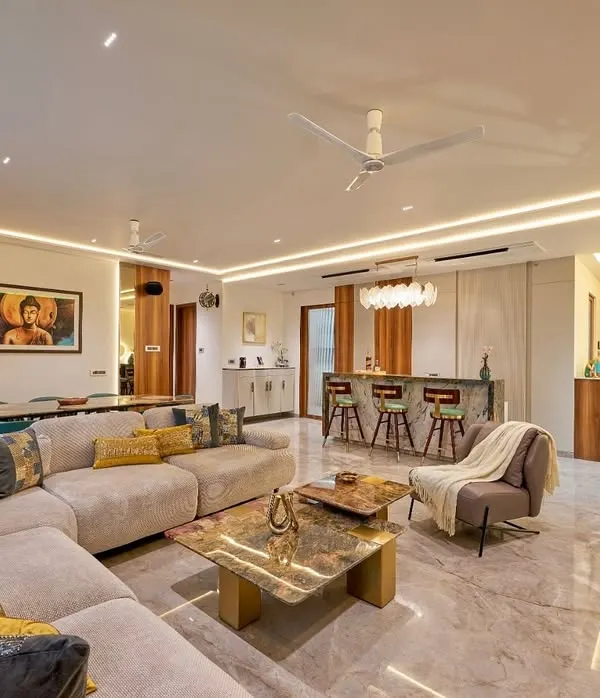 This open-plan residence showcases our expertise in creating harmonious living and dining spaces. We designed this area with a plush sectional sofa for comfort, a custom marble-top coffee table, and a stylish bar counter, all unified by sophisticated layered lighting to create an atmosphere of warm, inviting luxury.
