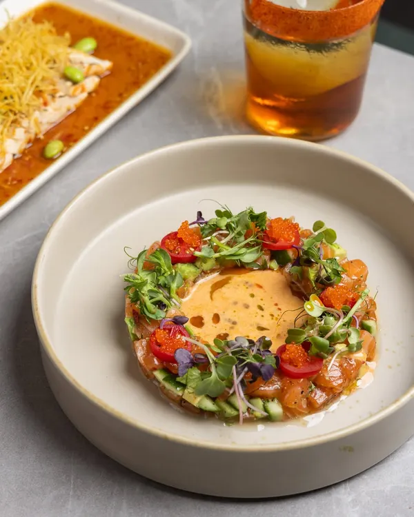 The beauty of a plate is in the details. Here, a salmon tartare is presented alongside a perfectly seared fish, showcasing how the sauce holds and the garnish finishes the dish.