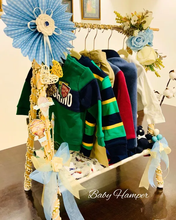 A close-up of our unique baby boy clothing rack hamper. This gift features a collection of stylish baby outfits, creatively displayed and decorated with blue ribbons and handcrafted details for a memorable presentation.