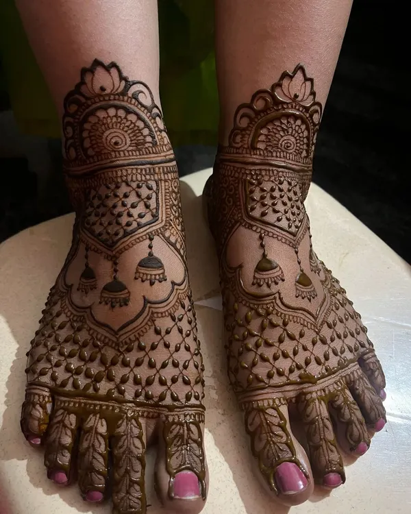 A full coverage foot mehendi featuring jhumka motifs and a delicate net pattern. This design provides a rich, traditional look for the bride's feet.