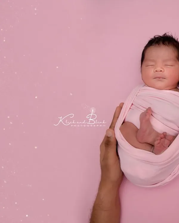 Held safely in her parents' hands. This classic newborn pose on a soft pink background highlights just how tiny and precious your baby is in their first few days.