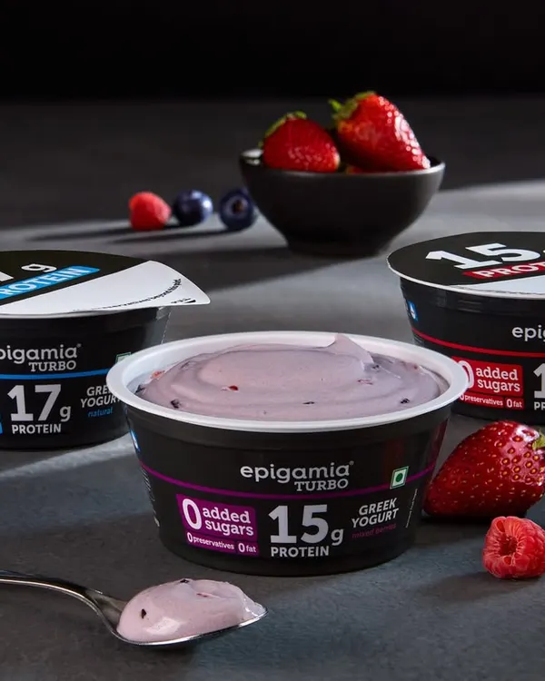 A clean product shot of Epigamia's Turbo protein yogurts. The focus here is on the creamy texture of the yogurt on the spoon and the fresh berry ingredients, communicating both taste and health.