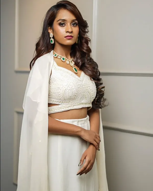 This all-white Indo-Western outfit features a beautifully textured crop top, a simple skirt, and a sheer, floor-length cape for a touch of drama.