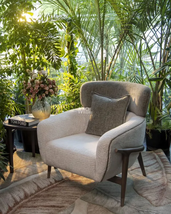 This is our Verdelle Armchair, a piece that truly embodies our design philosophy. Set against a backdrop of lush greenery, its design mirrors the tranquility of nature. We crafted the frame from solid ash wood for its durability and smooth grain, giving it a sculptural arm detail that nods to mid-century modern elegance. The soft, textured bouclé fabric is tactile and warm, making this more than just a seat, but a sanctuary.