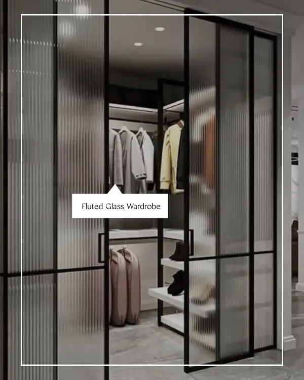 This walk-in closet features fluted glass sliding doors, offering a glimpse of the organized space within while adding a layer of texture and modern elegance. It is a perfect example of functional art.