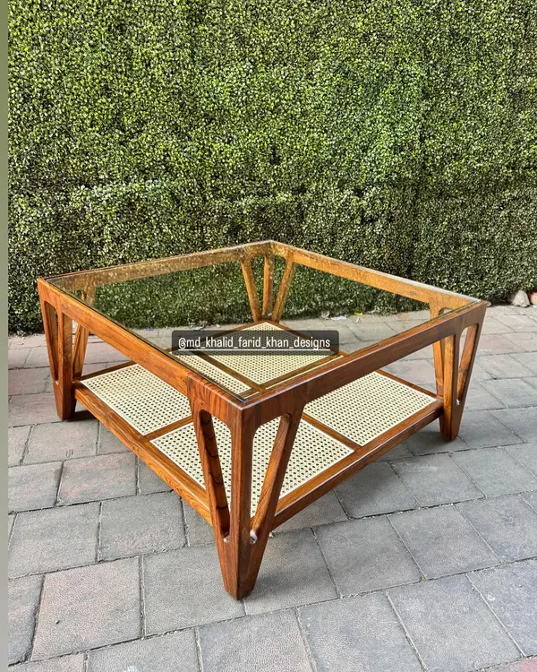 A beautiful mid-century inspired coffee table with a glass top and a lower shelf made of hand-woven cane. The angular, solid teak frame makes it a standout piece for any living room.