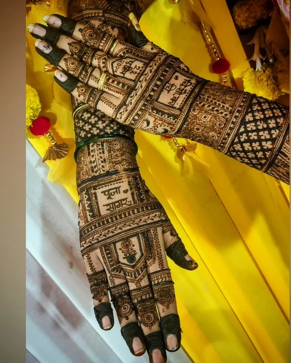 A beautiful bridal mehendi set against a vibrant yellow backdrop. This design features the couple's names, Pooja and Sagar, prominently on the palms, surrounded by traditional symbols and detailed jaali (net) patterns.