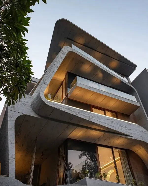 This home is a composition of cuboid and curvilinear volumes, punctuated by open balconies. The juxtaposition of sharp geometric shapes with organic forms creates a dynamic and visually engaging piece of architecture.