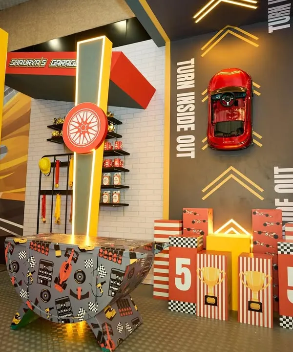 A themed game area within "Shaurya's Garage," featuring a bean bag toss and other activities designed with race car graphics and colors.