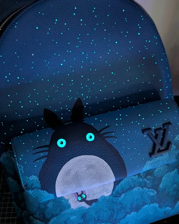 This custom Louis Vuitton backpack brings a classic Studio Ghibli scene to life. I used special glow-in-the-dark Angelus paints for Totoro's and Jiji's eyes, so the magic really comes out at night.