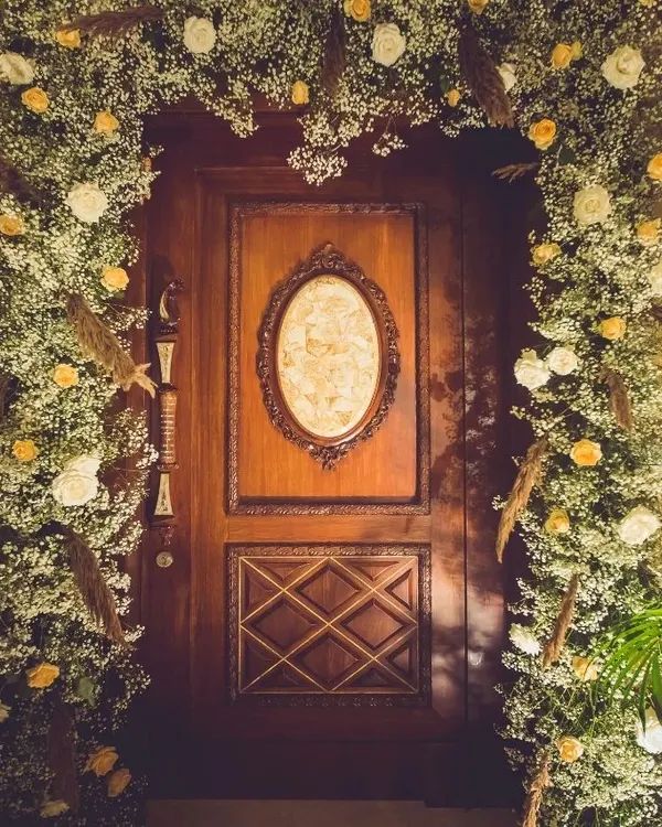 A grand doorway becomes a magical portal. We framed this beautiful wooden door with an arch of baby's breath, white roses, and dried pampas grass, creating an unforgettable entrance for a festive celebration.