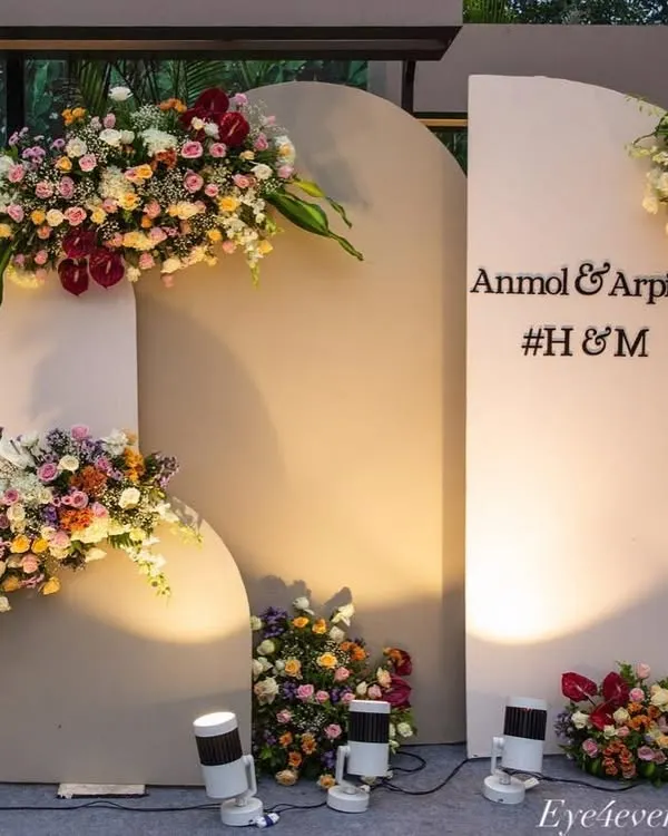 This modern and elegant photo backdrop features three arched panels in a neutral grey tone. The panels are decorated with lush, asymmetrical floral arrangements in vibrant colors and personalized with the couple's names.