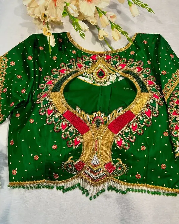This emerald green blouse is designed for a grand bridal look. It features a dramatic back cutout, intricate kundan and zardosi work, and peacock motifs on the flared sleeves.