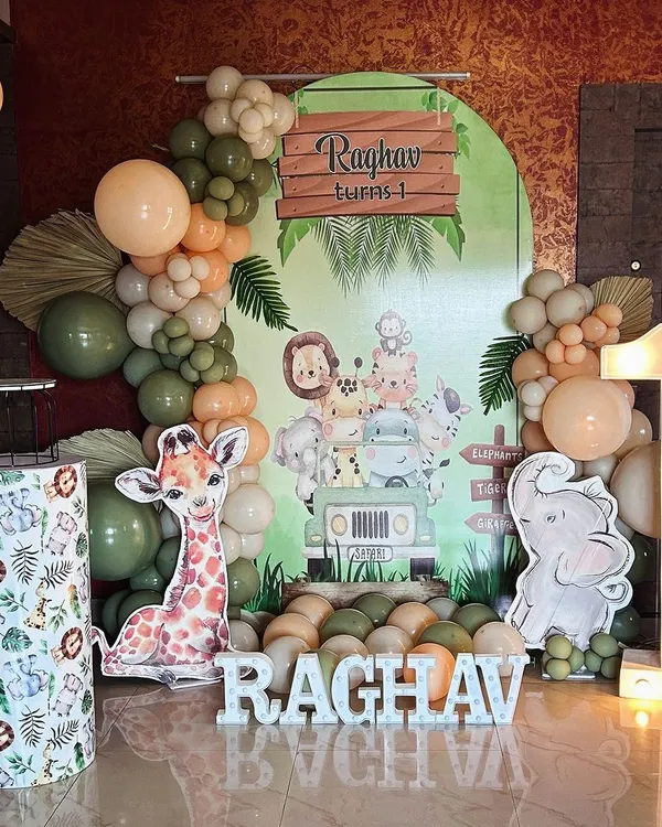 A complete safari-themed first birthday setup for Raghav, perfect for a home celebration. The decor includes a personalized backdrop, cute animal cutouts, a light-up number '1', and an organic balloon garland.