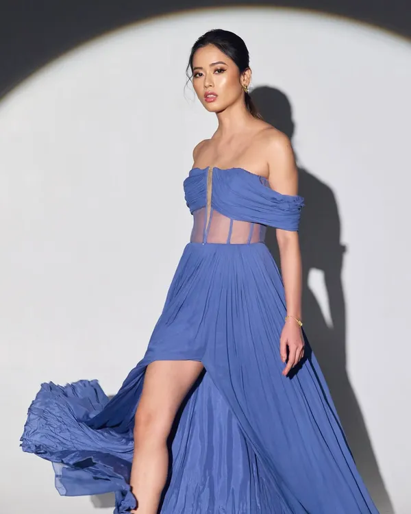 A full-length look from a fashion editorial. The makeup was designed to complement the flowing blue gown, with a focus on glowing skin and defined eyes that would stand out from a distance and draw attention to the model's expression.
