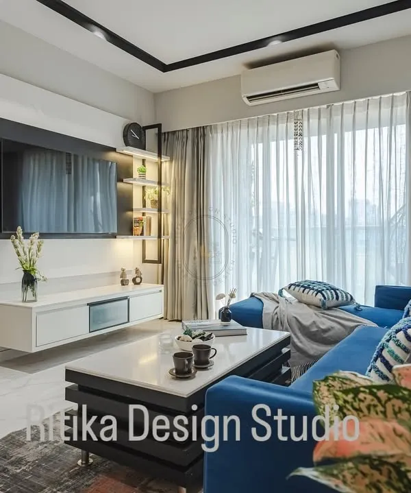 A close-up view of this modern living room highlights the contrast between the vibrant blue L-shaped sofa and the sleek black and white media unit. Sheer curtains allow for ample natural light, making the space feel bright and airy despite the bold color choices.