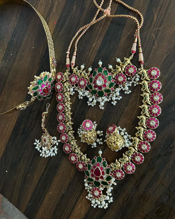 A beautiful Jadau-style set with red and green kemp stones and pearl clusters. This rental includes a choker, a longer necklace, maang tikka, and bajuband.