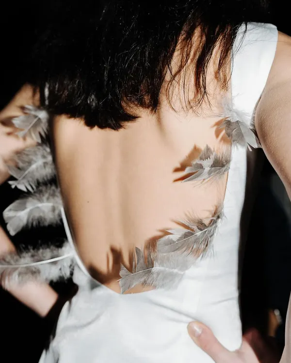 A detail shot from backstage at the A.W. Eber show during London Fashion Week. The focus is on the delicate feather details on the back of a white dress.