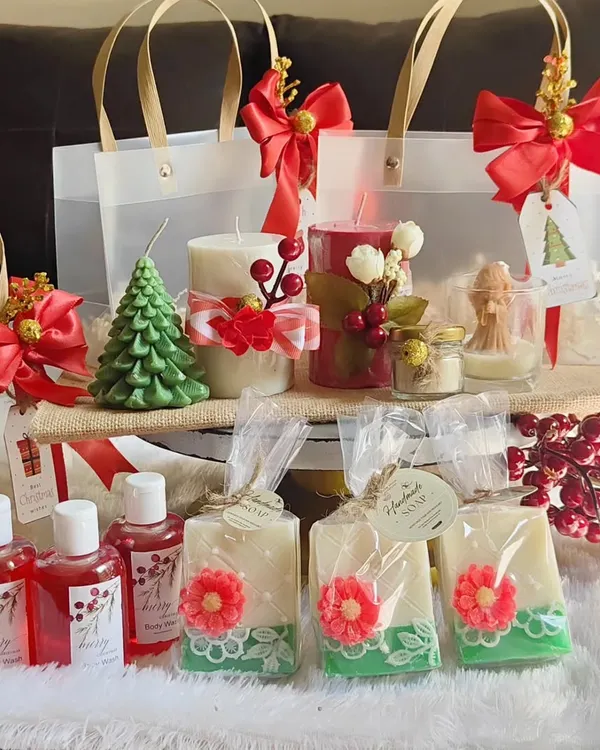 A full Christmas collection display, featuring tree and pillar candles, angel candles, handmade soaps, and body wash, all ready to be packed into festive gift bags.