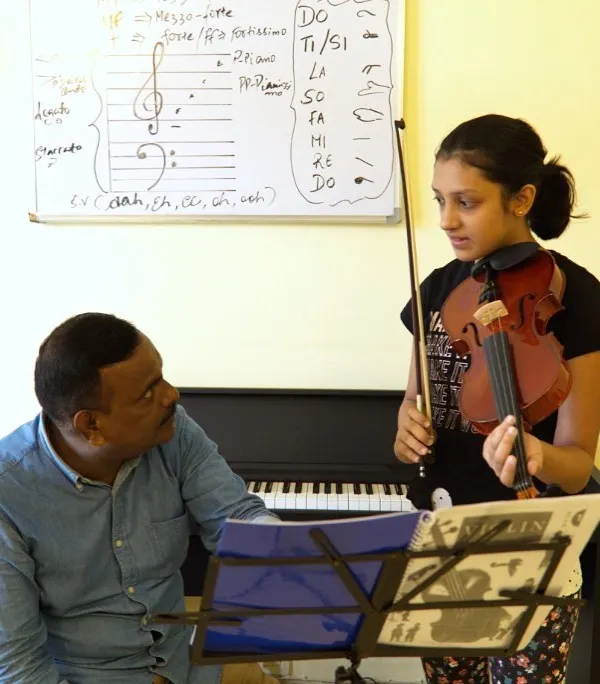 A violin training session is in progress at our Gurugram conservatory. Here, an instructor provides feedback to a student, with music theory notes visible on the whiteboard, showing our integrated approach to learning.
