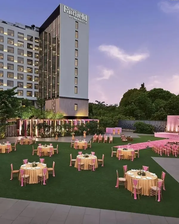 This image shows a grand lawn setup for a pastel-themed wedding. The pink stage and seating arrangements look stunning against the green lawn and the modern hotel backdrop, creating a picture-perfect scene.