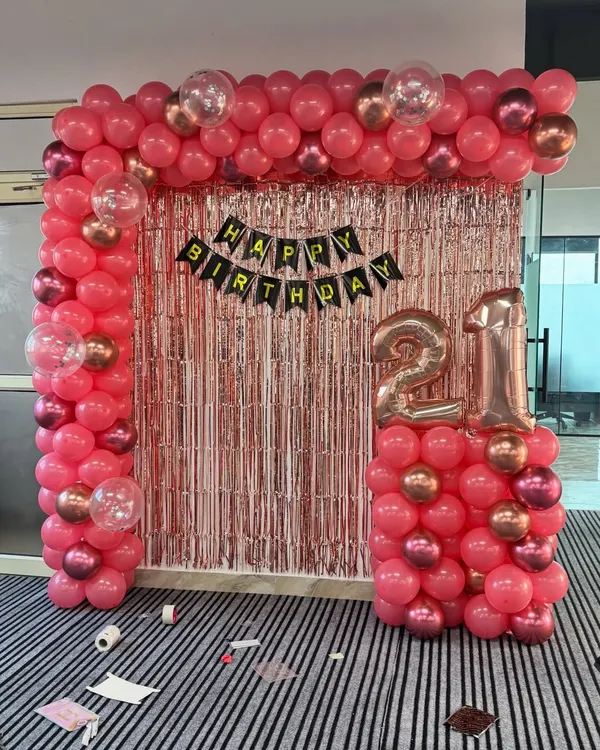 A complete 21st birthday setup in an office. The theme uses a popular pink and rose gold color scheme with a full balloon arch and number foils.