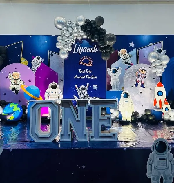 A spectacular outer space theme for a "First Trip Around The Sun." The entire stage is transformed into a galaxy with a star-studded floor, planet cutouts, astronaut figures, rockets, and a large "ONE" marquee table.