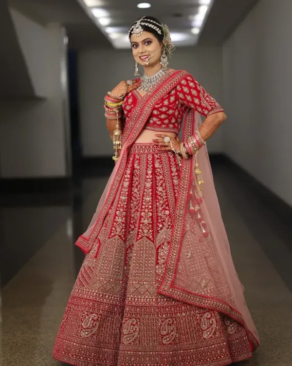 A full-length view of this gorgeous bride in her red and pink lehenga. The complete look, from the detailed makeup to the elegant hair and draping, creates a picture-perfect bridal moment.